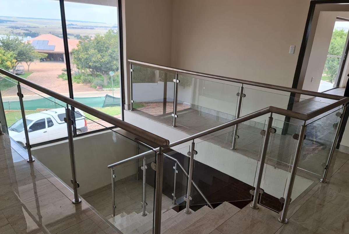 Frameless glass balustrade with a brushed stainless steel handrail overlooking a marble staircase landing, with a countryside view through floor-to-ceiling windows