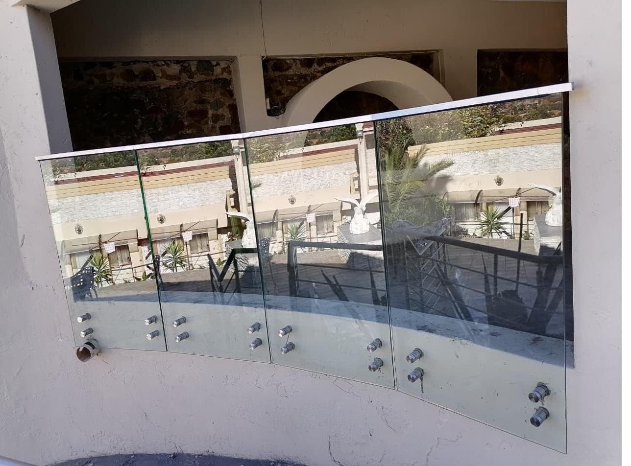 Curved frameless glass balustrade panels on spigot fittings along a resort-style terrace