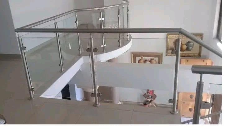 Curved frameless glass balustrade with brushed stainless steel handrail on an upper landing